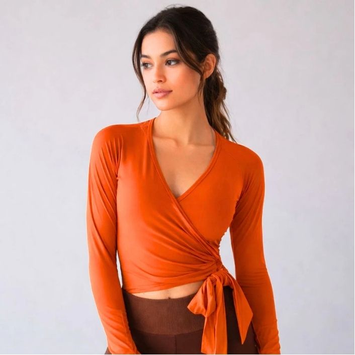 Woman wearing an orange long-sleeve top with a knot detail on a white background